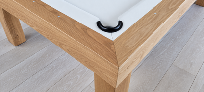 Close-up of the Rift pool table’s mitered white oak corner, black pocket, white felt, and rail sights.